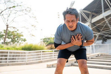 Senior asian man tired during jogging at outdoor sport stadium. Mature asian male intense training workout challenge breathing exhausted. Healthy and activity lifestyle concept.