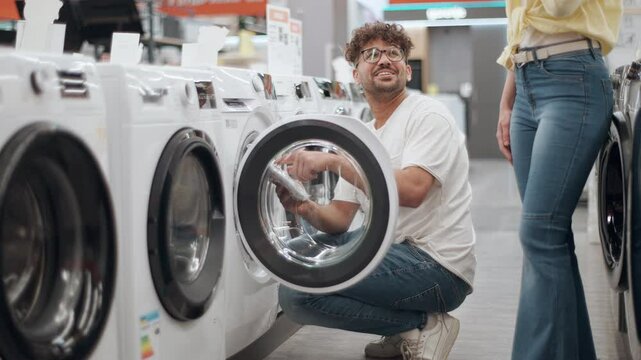 Happy couple choosing washing machine in electronics store. Young couple browsing home appliance store, comparing washing machine features with cheerful interaction.