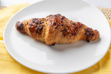 Delicious chocolate croissant resting on white plate and yellow napkin