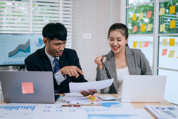 Cheerful Asian businessman and woman looking at laptop screen, analyzing project success in office.