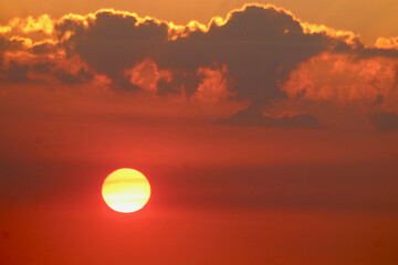 The disk of the setting sun against the background of orange sky and clouds. The sun moves down passing through thick clouds against the background of orange sky. Sunset background.