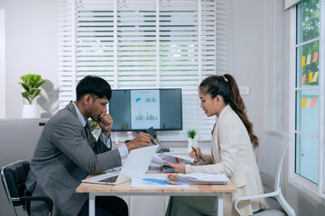 Cheerful Asian businessman and woman looking at laptop screen, analyzing project success in office.