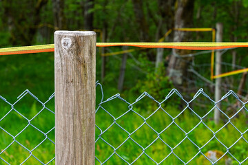 A sturdy wooden fence post supports vibrant tape that outlines a property boundary surrounded by...