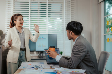 Cheerful Asian businessman and woman looking at laptop screen, analyzing project success in office.