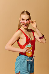 Vibrant young woman enjoying a refreshing drink with playful style against a warm backdrop