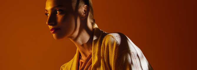 Young beautiful woman in trendy outfit poses against warm backdrop during a stylish photoshoot