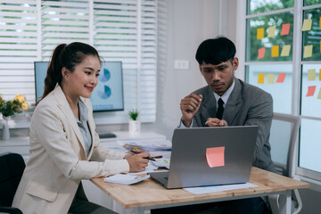 Fototapeta premium Cheerful Asian businessman and woman looking at laptop screen, analyzing project success in office.