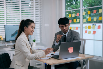 Obraz premium Cheerful Asian businessman and woman looking at laptop screen, analyzing project success in office.