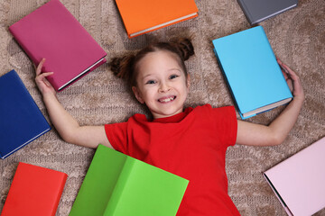 Cute girl with many different books on rug at home, top view