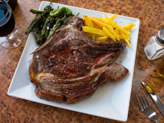 Grilled beef chop on the bone, served with a vegetable side dish of fried potatoes and green padron peppers