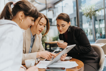 Three women in professional attire discussing ideas in a business setting over coffee.