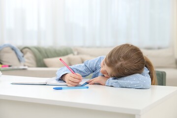 Naklejka premium Tired little girl doing homework at table indoors