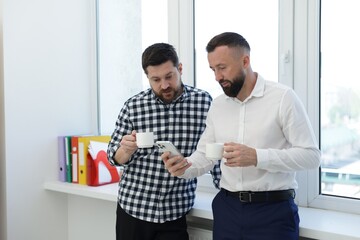Fototapeta premium Colleagues with coffee and smartphone during lunch break in office