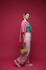 Fashionable full-length portrait of beautiful woman in stylish outfit on dark red background