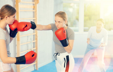 Young female co-participant and woman sparring partners during training battle fight using technique of boxing match under supervision of woman instructor. Boxing section for women, sport as lifestyle
