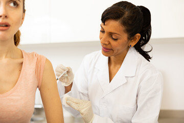 Obraz premium Portrait of positive woman doctor injecting shot of vaccine to female patient at clinic