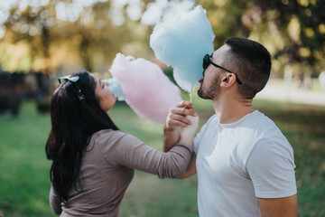 A happy young couple sharing pink and blue cotton candy outdoors. They are enjoying a fun, carefree...