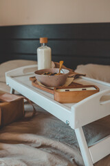 Stylish breakfast tray with a bowl of granola, milk bottle, and candle on a cozy bed, next to a beautifully wrapped gift. A calm and warm morning celebration scene
