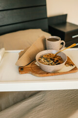 Flatlay of cozy breakfast tray with granola, milk, amber candle, and napkin on a soft beige bed. Warm tones and natural textures create a calm and peaceful morning scene
