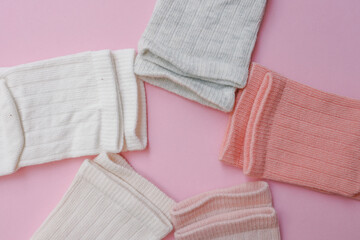 Flat lay of baby socks in soft pastel tones—white, peach, coral, and grey—arranged in a circular composition on a pink background. Cozy and gentle aesthetic perfect for infant apparel display