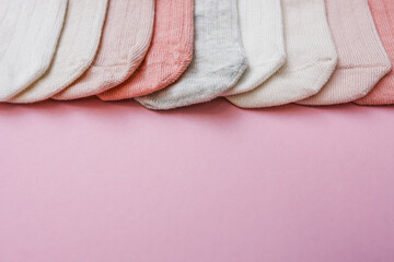 Set of soft cotton baby socks in pastel colors including white, pink, peach, and grey, neatly arranged on a pink background. Flat lay composition with minimal style