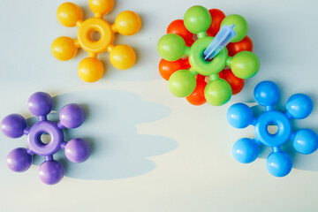 Colorful plastic construction toys with circular arms scattered on a white background. A toddler’s hand reaching out to touch them, evoking creativity and early learning through play