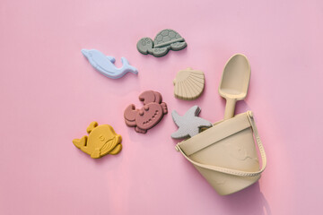 Set of pastel silicone beach toys arranged on pink background, including dolphin, crab, turtle, starfish, fish, seashell, bucket, and shovel in minimalistic eco-friendly style