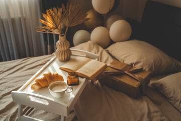 Elegant morning scene with coffee, croissant, book, gift box, dried palm leaves, and balloons on a...