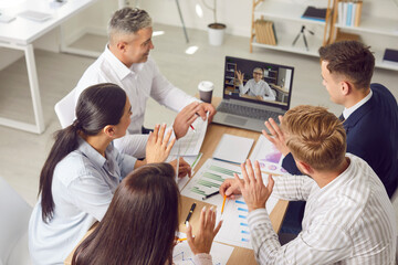 Team of people meeting in office and having conference call with colleague. Group of men and women sitting together at table looking at screen of laptop computer. Online business communication concept