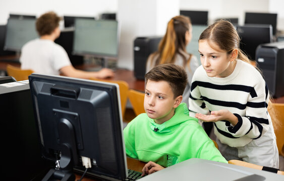 Schoolboy helping girl, his classmate, to find solution of computer trouble in classroom.