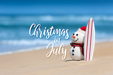 Christmas in July sale template design with a snowman on a beautiful beach, standing with a surf board.