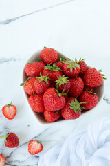 Fresh strawberries in a heart shaped bowl on white marble background. Top view. Copy space.