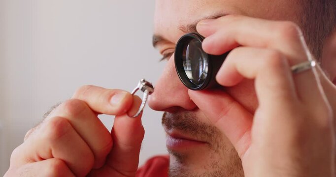 Man uses magnifying glass monocular to evaluate ring, looking for flaws or unique characteristics. Professional goldsmith manufacturing or repair luxury wedding engagement ring. Jewelry art concept.