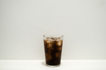 Iced coffee americano in a tall glass with ice cubes on white background.