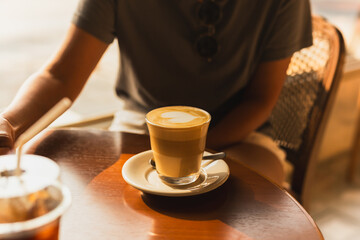 Woman with hot latte glass on the table in cafe with sun light.