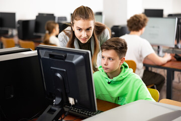 Fototapeta premium Friendly female teacher consulting interested concentrated tween boy studying in information technology class..