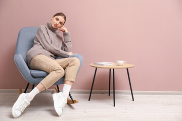 Beautiful woman relaxing in comfortable rocking chair near beige wall indoors