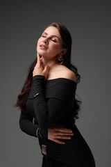 Young woman in stylish black dress on grey background