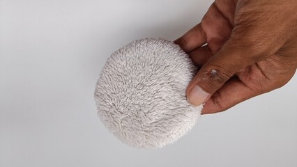 Hand holding a fluffy white cosmetic applicator puff, showcasing the soft texture for gentle makeup and skincare routines.