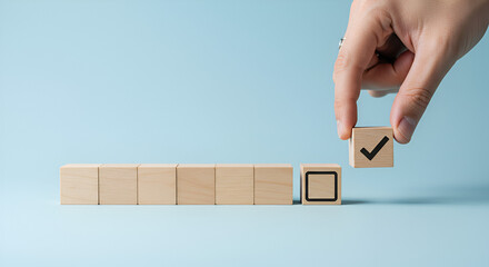 Close-up of a hand holding a wooden block featuring a checkmark, positioned beside another block with a blank square, set on a pastel blue backdrop.