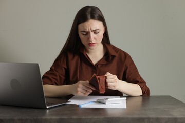 Upset woman with empty wallet at grey table. Financial problems