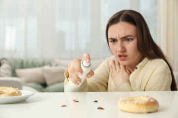 Emotional young woman spraying insecticide onto cockroaches at white table indoors, selective focus. Pest problem