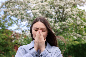 Woman suffering from seasonal pollen allergy near blossoming tree on spring day