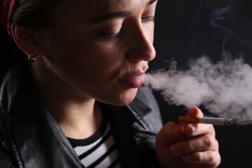 Woman smoking cigarette on black background, closeup