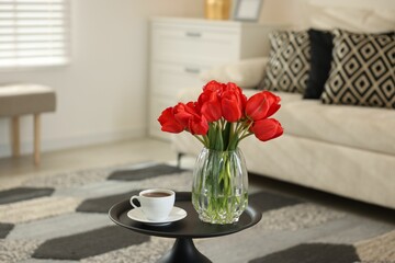Beautiful red tulips in vase and tea on table indoors