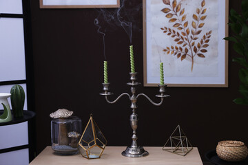Elegant candlestick with candles and decor on table near brown wall