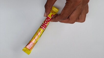 A person's hand holding a colorful sachet of a sweet candy stick, a convenient portable snack for...