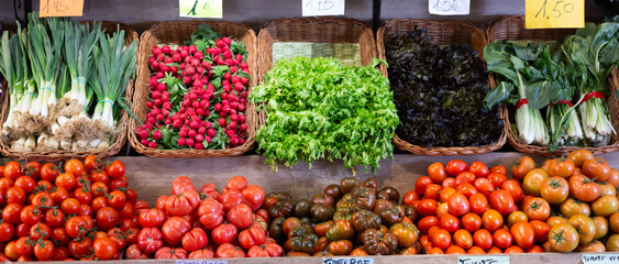 Fresh seasonal vegetables on the counter of a grocery store. Farm tomatoes, leeks, radishes and lettuce in the supermarket. Choosing organic vegetables and greens