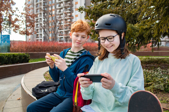 Young boy and girl playing video games on their smart phones in a park after skipping school