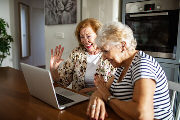 Senior lesbian couple laughing while video chatting with family on laptop at home